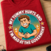 Majica z napisom MY TUMMY HURTS AND I'M MAD AT THE GOVERMENT in humorističnim risanim motivom moškega, ki se drži za trebuh