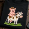 Majica z ilustracijo prašiča v kavbojskem klobuku, ki jezdi belo kravo z rjavimi lisami