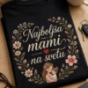 Ženska majica z napisom "Najboljša mami na svetu" v elegantni script tipografiji, z nežnimi divjimi rožami in malim rdečim srcem na temnem ozadju.